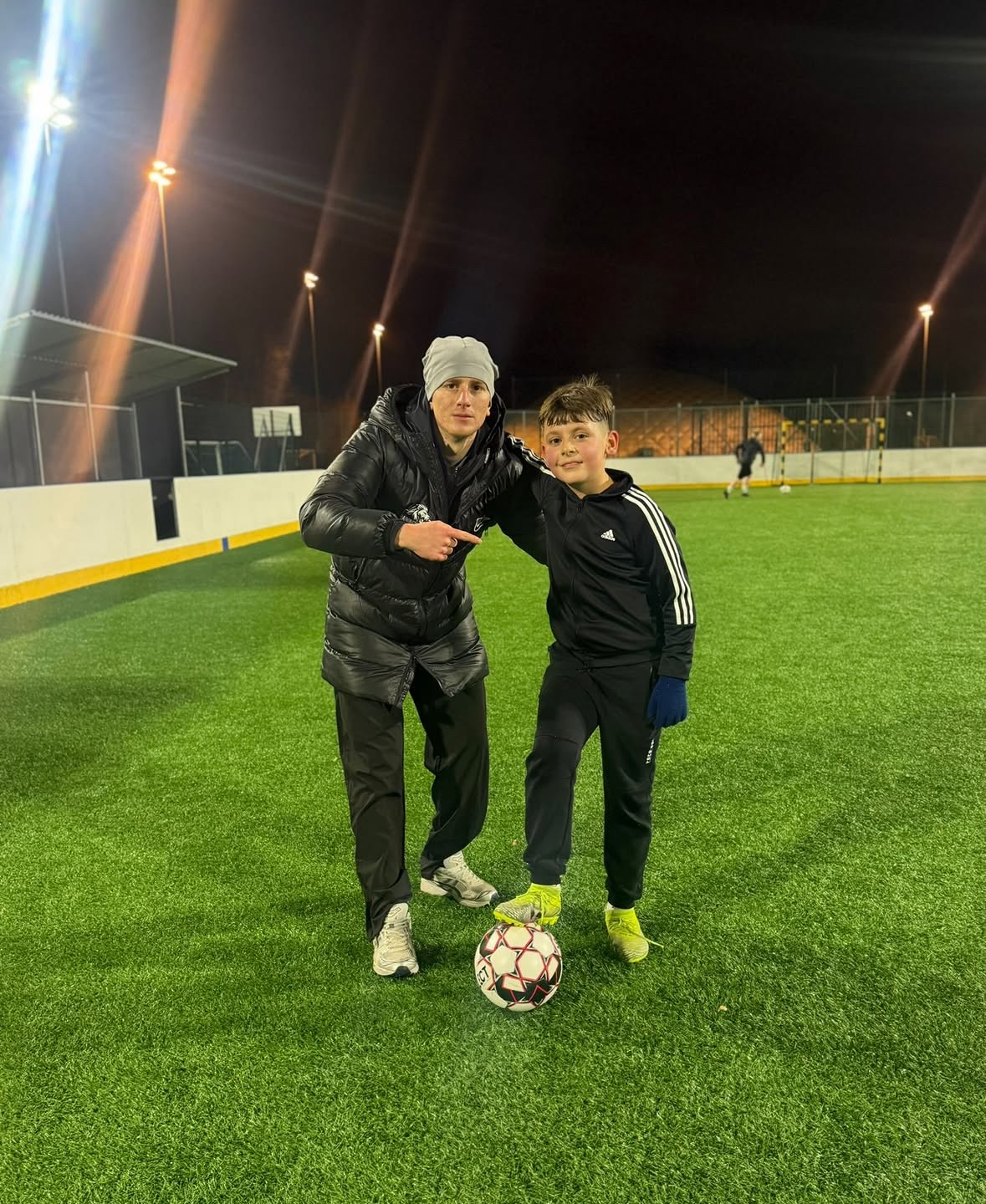 Valmentaja ja nuori pelaaja poseeraavat pallon kanssa kentällä